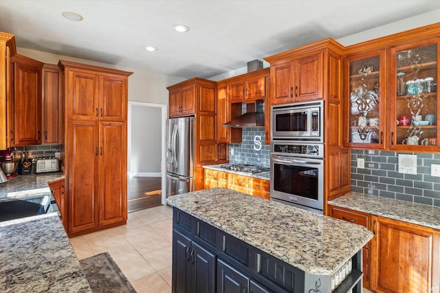 kitchen with backsplash, stainless steel appliances, a center island, light stone countertops, and wall chimney exhaust hood