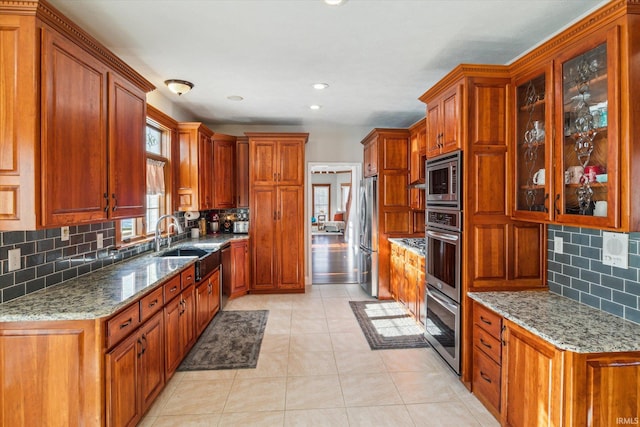 kitchen with tasteful backsplash, stainless steel appliances, light stone countertops, and sink