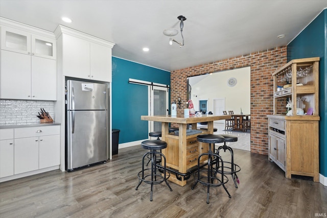 kitchen featuring brick wall, dark hardwood / wood-style floors, stainless steel refrigerator, white cabinetry, and a barn door