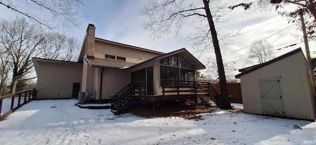 snow covered back of property with a sunroom, central AC, a deck, and a storage unit