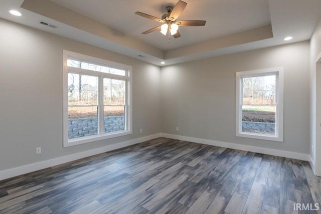 empty room with dark hardwood / wood-style flooring, a raised ceiling, and ceiling fan