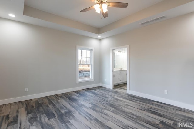 empty room with dark wood-type flooring, a raised ceiling, and ceiling fan