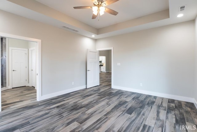 empty room with dark wood-type flooring, a raised ceiling, and ceiling fan