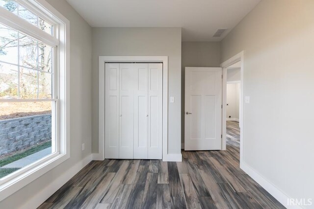 unfurnished bedroom with multiple windows, dark hardwood / wood-style flooring, and a closet