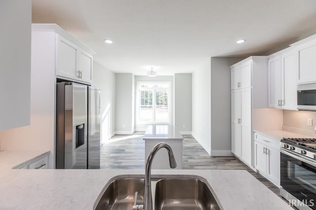 kitchen featuring sink, white cabinetry, hardwood / wood-style floors, stainless steel appliances, and light stone counters