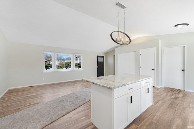 kitchen featuring white cabinetry, a center island, vaulted ceiling, pendant lighting, and light stone countertops