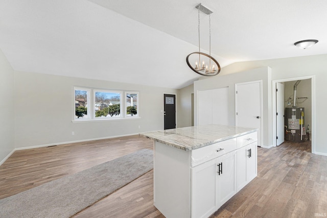 kitchen featuring gas water heater, white cabinetry, light stone counters, decorative light fixtures, and vaulted ceiling