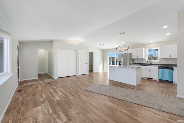 kitchen featuring white cabinetry, lofted ceiling, hanging light fixtures, a center island, and stainless steel appliances