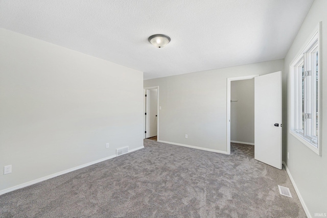 unfurnished bedroom featuring a walk in closet, carpet floors, a textured ceiling, and a closet