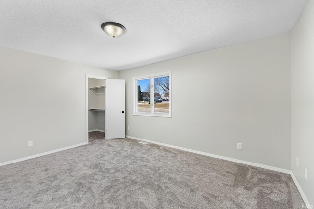 unfurnished bedroom featuring carpet floors, a spacious closet, a textured ceiling, and a closet