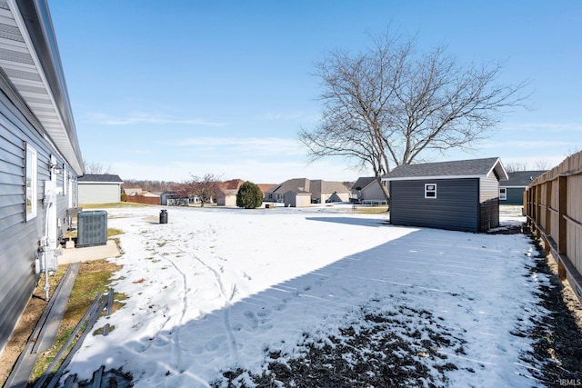 yard layered in snow featuring a shed and central AC