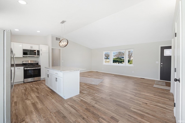 kitchen with a kitchen island, appliances with stainless steel finishes, pendant lighting, lofted ceiling, and white cabinets