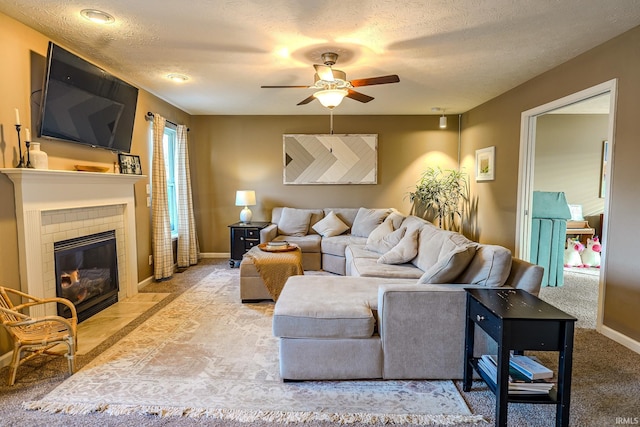 carpeted living room with ceiling fan, a tiled fireplace, and a textured ceiling