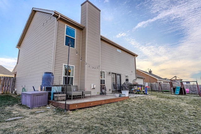 back house at dusk featuring a yard, a playground, and a deck