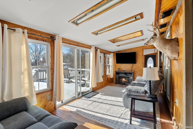 living room with hardwood / wood-style floors, wooden walls, lofted ceiling with skylight, and a fireplace