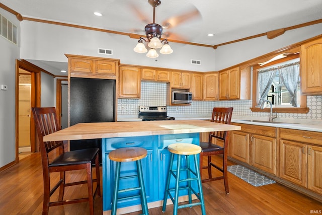 kitchen featuring a breakfast bar, appliances with stainless steel finishes, ornamental molding, a kitchen island, and wood counters