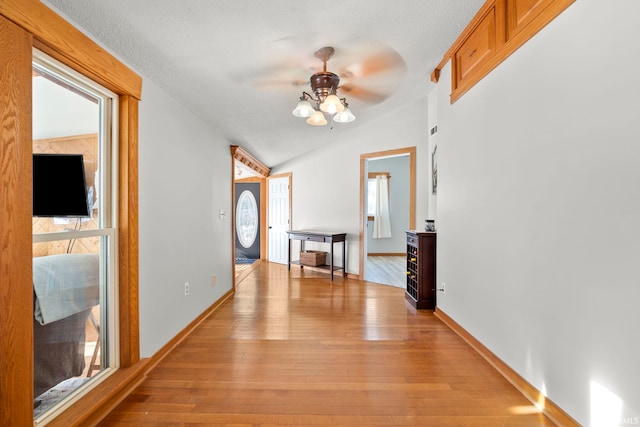 hallway featuring lofted ceiling, a textured ceiling, and light hardwood / wood-style flooring