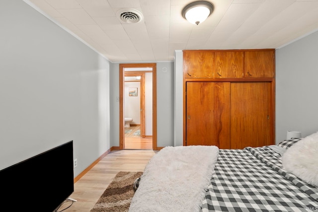 bedroom featuring light hardwood / wood-style flooring, ornamental molding, and a closet