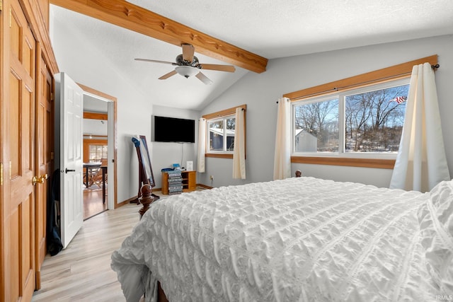 bedroom featuring lofted ceiling with beams, light wood-type flooring, a textured ceiling, and ceiling fan