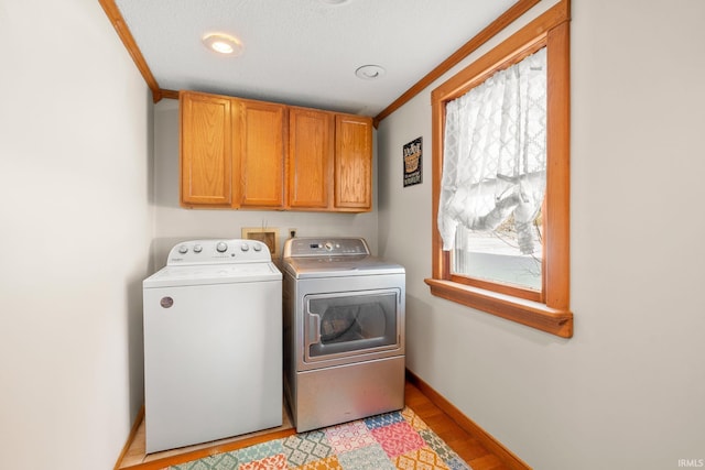 laundry area with cabinets, ornamental molding, washer and dryer, and a healthy amount of sunlight