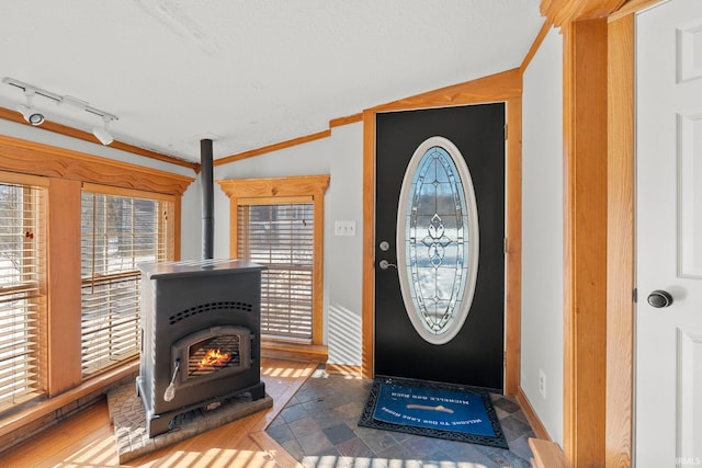 entrance foyer featuring ornamental molding, vaulted ceiling, and a wood stove