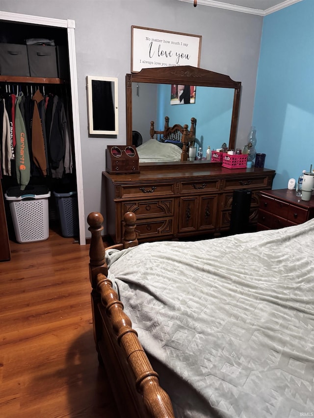 bedroom with wood-type flooring, ornamental molding, and a closet