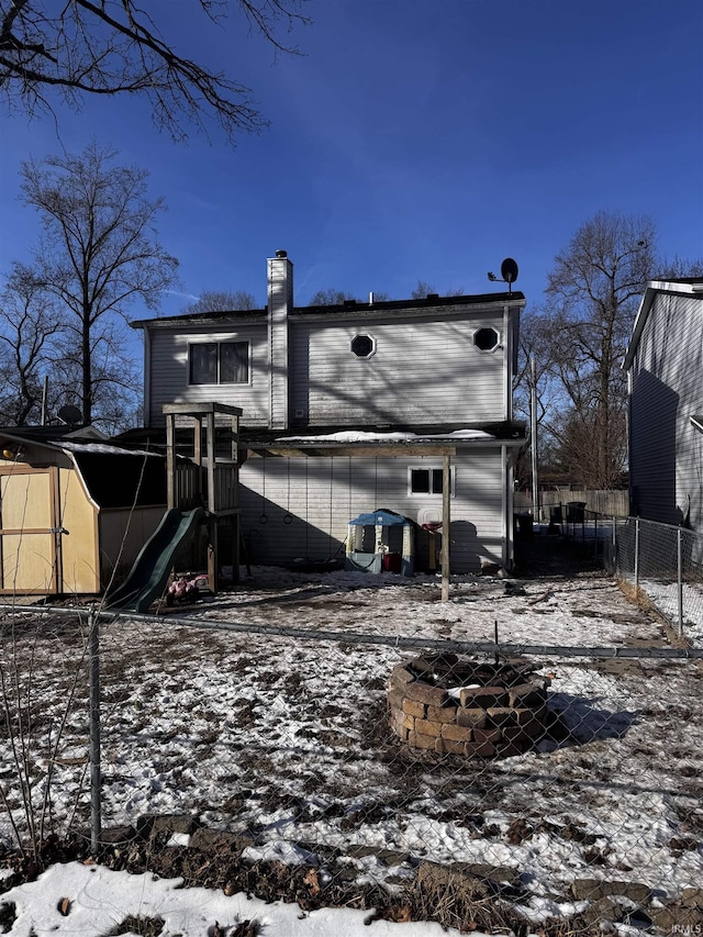 snow covered rear of property with a storage shed, a fire pit, and a playground