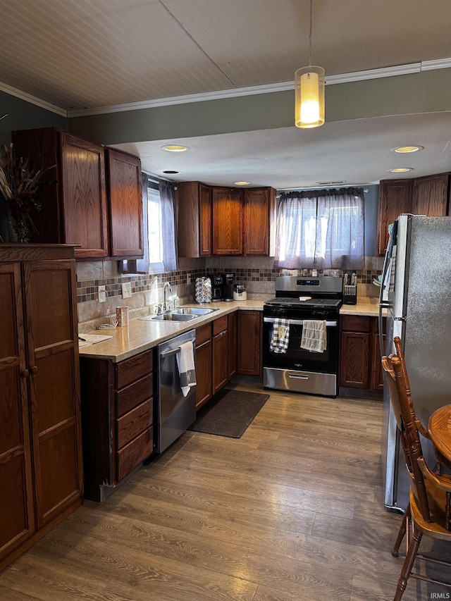 kitchen with sink, decorative light fixtures, ornamental molding, appliances with stainless steel finishes, and hardwood / wood-style flooring