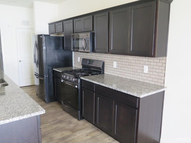 kitchen featuring dark brown cabinetry, light wood-type flooring, light stone countertops, decorative backsplash, and black appliances