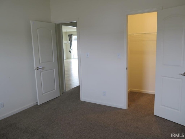 unfurnished bedroom with a spacious closet, dark carpet, and a closet