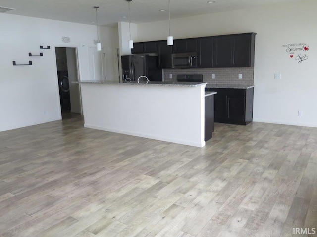 kitchen featuring pendant lighting, backsplash, black fridge, light hardwood / wood-style floors, and light stone countertops