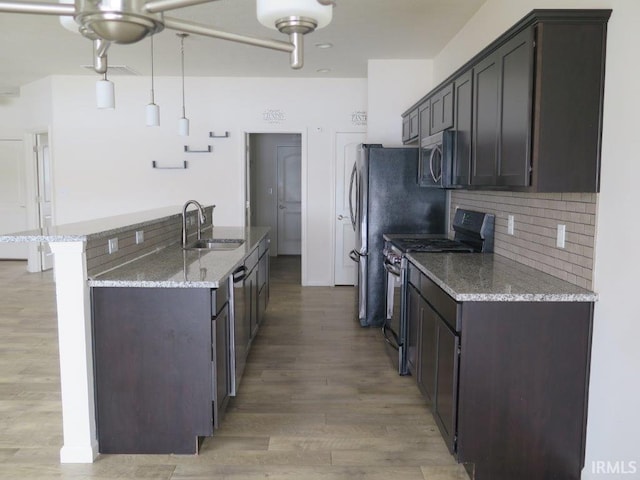 kitchen featuring appliances with stainless steel finishes, decorative light fixtures, sink, dark brown cabinetry, and light stone counters