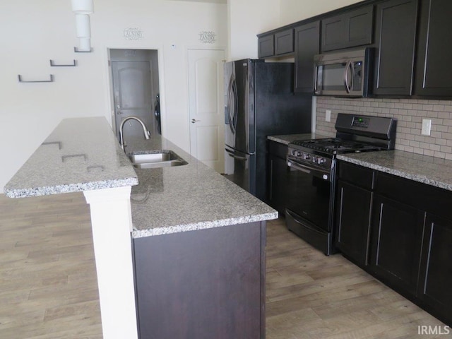 kitchen with an island with sink, light stone countertops, sink, and black appliances