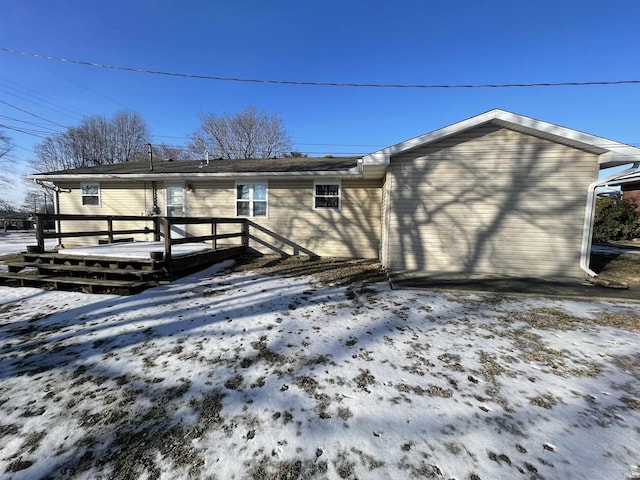 snow covered back of property with a wooden deck