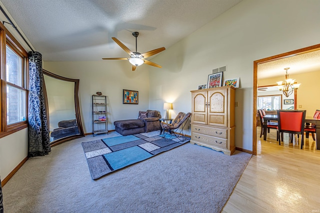 living room with lofted ceiling, ceiling fan with notable chandelier, a textured ceiling, and light wood-type flooring