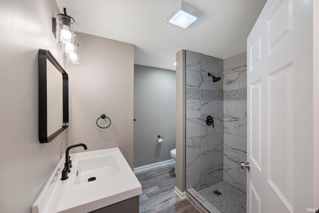 bathroom with tiled shower, wood-type flooring, toilet, and vanity