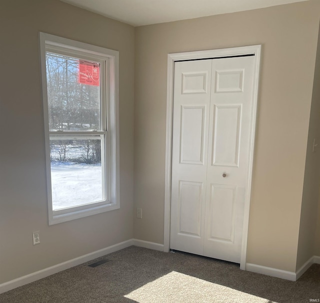 unfurnished bedroom featuring a closet, dark carpet, and multiple windows