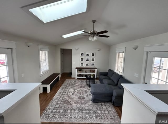 living room with dark wood-type flooring, vaulted ceiling with skylight, and ceiling fan