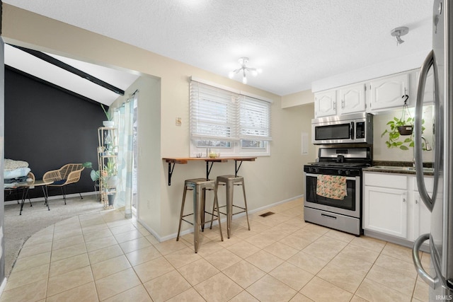 kitchen featuring lofted ceiling, a textured ceiling, light tile patterned floors, stainless steel appliances, and white cabinets