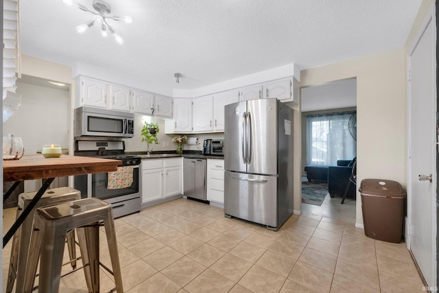 kitchen featuring appliances with stainless steel finishes, white cabinetry, sink, light tile patterned floors, and a textured ceiling