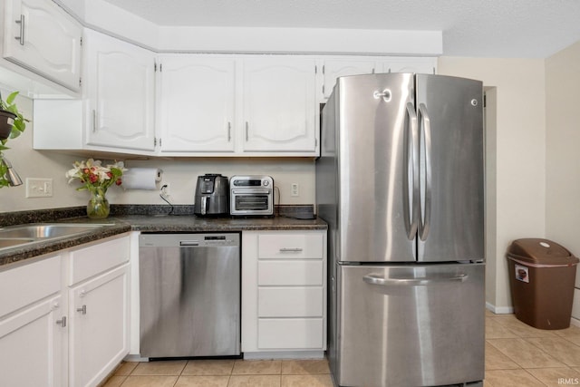 kitchen featuring stainless steel appliances, white cabinetry, dark stone countertops, and light tile patterned flooring