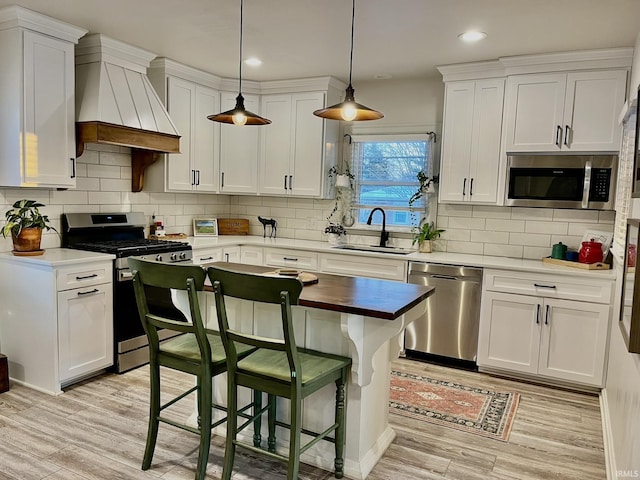 kitchen featuring sink, premium range hood, white cabinetry, appliances with stainless steel finishes, and decorative light fixtures