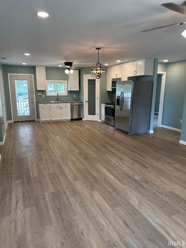 kitchen featuring appliances with stainless steel finishes, ceiling fan with notable chandelier, decorative light fixtures, white cabinetry, and hardwood / wood-style flooring