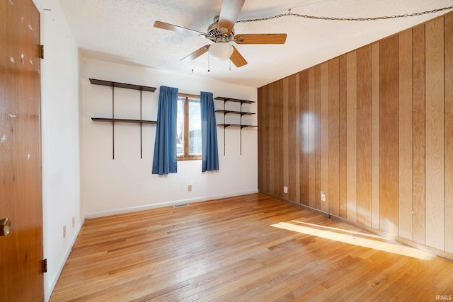 unfurnished room with ceiling fan, light hardwood / wood-style floors, a textured ceiling, and wood walls