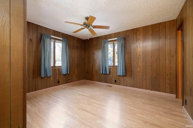 spare room featuring ceiling fan, plenty of natural light, and wood walls