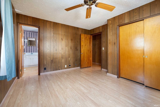 unfurnished bedroom featuring wooden walls, light hardwood / wood-style floors, a closet, and ensuite bathroom