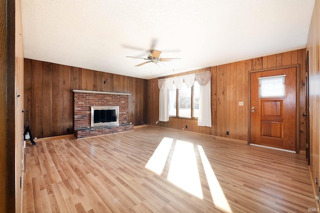 unfurnished living room with ceiling fan, a fireplace, light hardwood / wood-style floors, and wood walls