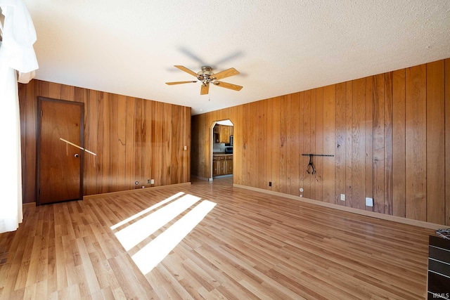 spare room with ceiling fan, wood walls, a textured ceiling, and light wood-type flooring