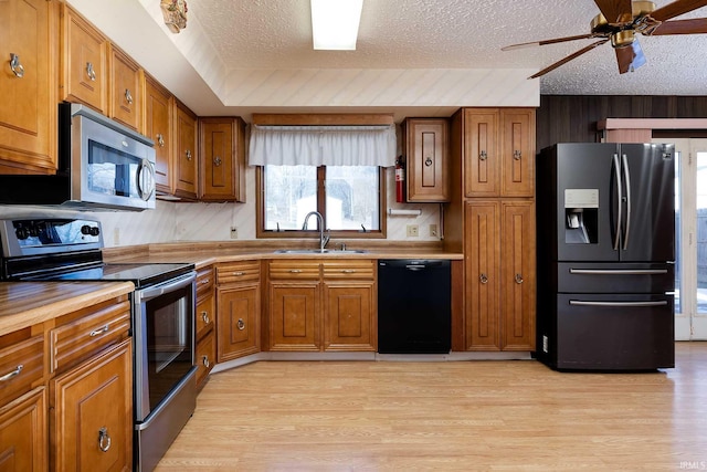 kitchen with appliances with stainless steel finishes, sink, a textured ceiling, and light hardwood / wood-style flooring