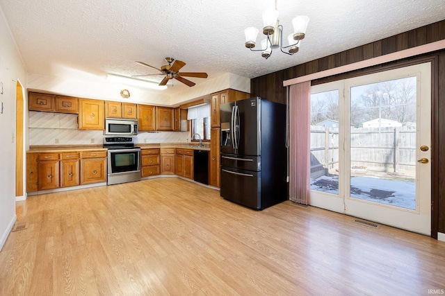 kitchen featuring ceiling fan with notable chandelier, decorative light fixtures, light hardwood / wood-style floors, black appliances, and a textured ceiling